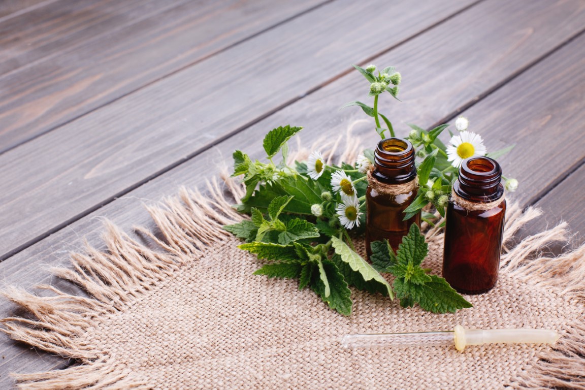 Brown bottles with oils, greenery and flowers lie on brown napkin